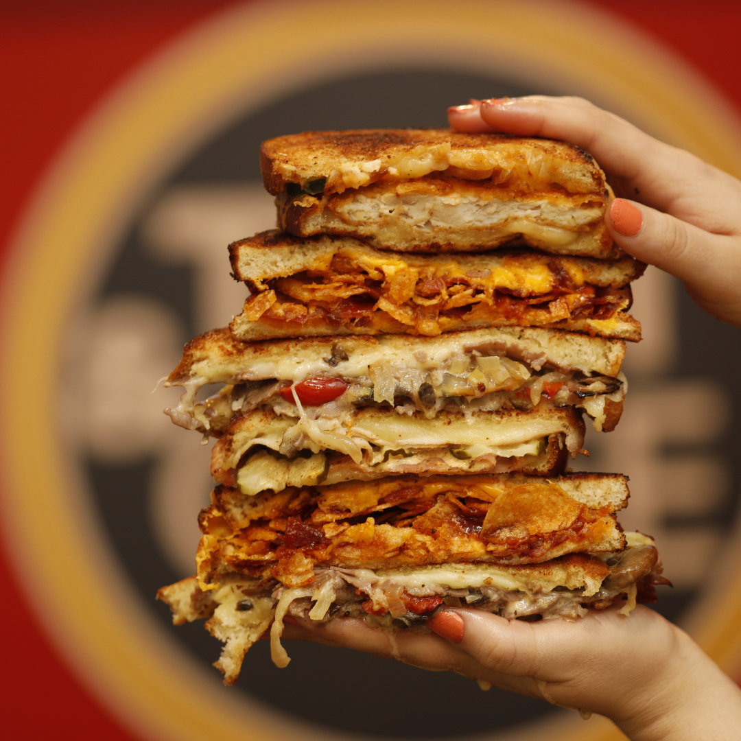 Stack of grilled cheeses in front of the Tom & Chee logo